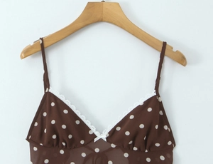 Detail of polka dot camisole with white lace trim and bow on dark brown fabric