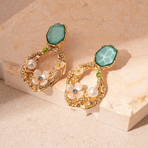 Detailed shot of vintage gold earrings with cyan gemstone, white flower and pearls