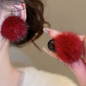 Détail des boucles d'oreilles pompons bordeaux avec une texture douce et veloutée