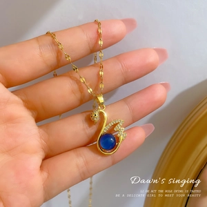 Detailed view of swan pendant featuring blue stone and pavé zircon on golden chain