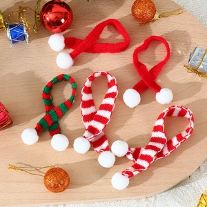 Close-up of five miniature knitted Christmas scarves with festive pom-poms on wood surface