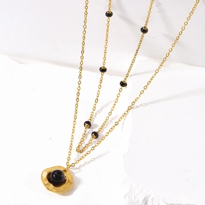 Double-layered gold necklace with black beads and a sunburst pattern pendant