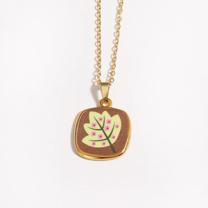Macro shot of gold square pendant with brown enamel leaf and pink floral painting