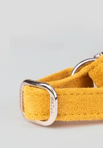 Detailed macro view of yellow suede pet harness with silver metal buckle and engraved logo