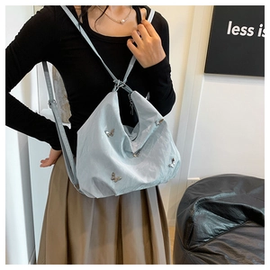 On-body view of a light blue pleated tote bag featuring silver metal butterfly accents