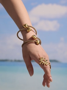 Detail of golden hollow heart mesh bracelet and sun ring on model at the beach