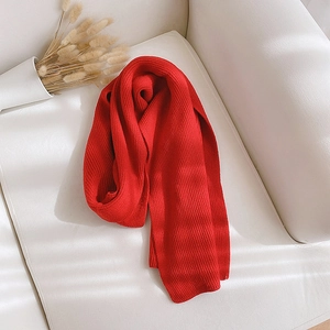 Detail of soft red knitted winter scarf elegantly placed on a white leather sofa