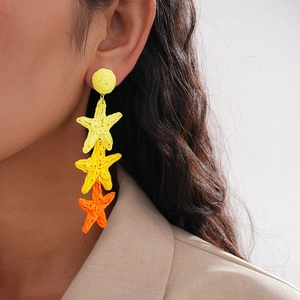 Macro shot of yellow and orange raffia star fringe earrings on a model profile