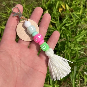 Détail d'un porte-clés perlé avec perles en silicone vertes, médaillon en bois et pompon blanc
