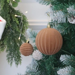 Brown velvet ribbed Christmas ball ornaments with gold hangers on a festive flocked tree