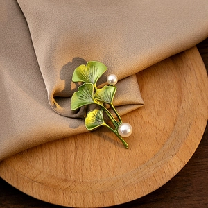 Detail view of green enamel ginkgo leaf brooch with white pearls on beige fabric background