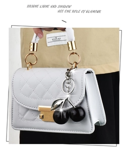 Detail of white quilted handbag featuring gold hardware and a black cherry charm