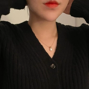 Close-up of white teardrop pearl pendant with delicate gold chain on a black sweater
