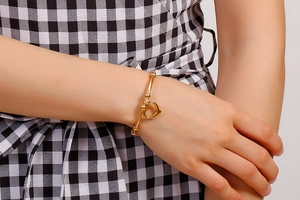 Close-up of a gold heart charm bracelet on a wrist, featuring a hollow heart pendant