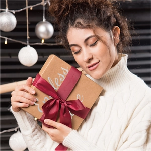 Brown kraft gift box with red ribbon and glitter letters held in a festive setting