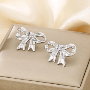 Close-up of silver bow-shaped stud earrings on beige silk fabric with high quality metal texture