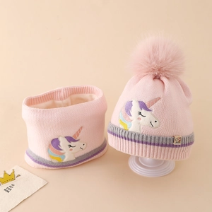 Detail of pink knitted hat and scarf set featuring embroidered unicorn and pom-pom