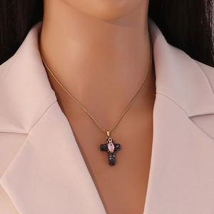 Detailed close-up of a gold cross pendant necklace with pink gem on a female model