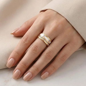 Dettaglio di un anello dorato a conchiglia con pavé di diamanti e intarsio in smalto bianco