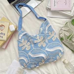 Dettaglio della borsa tote azzurra con ricamo floreale bianco e bordi con nappe