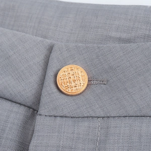 Bouton en métal doré avec motif de treillis sur une veste de tailleur grise