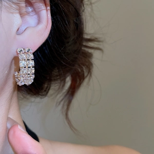 Close-up of golden C-shaped hoop earrings with double row of clear cubic zirconia crystals