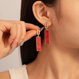 Detail of red geometric rectangular drop earring with gold trim worn by a model