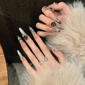 Dettaglio delle unghie stiletto cat-eye argento con cristalli neri e decorazione a fiocco