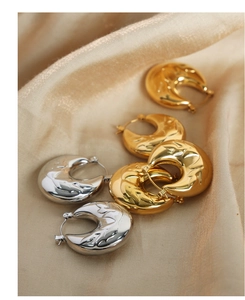 Macro shot of U-shaped gold and silver earrings with vintage embossed textures on silk