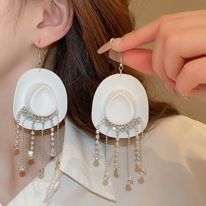 Detail of white cowboy hat earrings with sparkling rhinestone tassels worn on ear