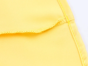 Close-up of yellow satin dress fabric with neat edge stitching and overlock hem detail