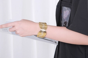 Detail of a gold-plated open cuff bracelet featuring shimmering rhinestone patterns