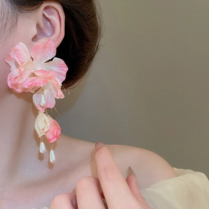 Detail of pink fabric flower earrings with long pearl tassels worn by a model