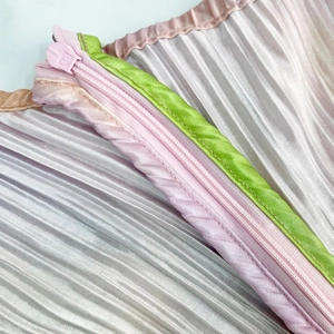 Macro detail of pleated satin dress showing the pink zipper and green contrast piping