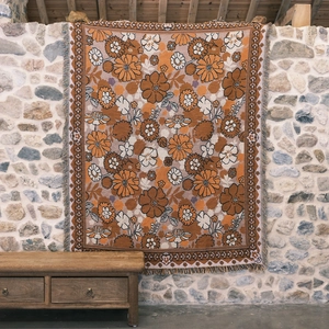 Close-up of retro floral woven blanket with fringe texture on a stone wall backdrop