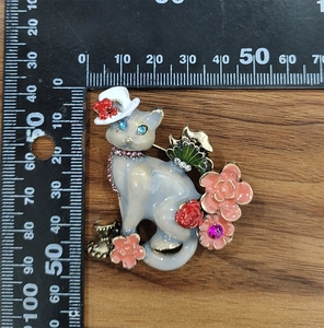 Detail view of a vintage cat brooch with enamel flowers and rhinestones on wood surface