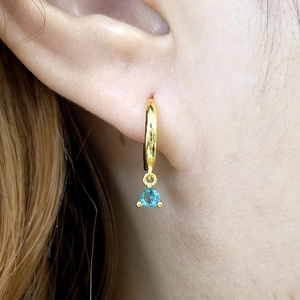 Detail of 925 silver gold earring with light blue zircon drop pendant on model ear