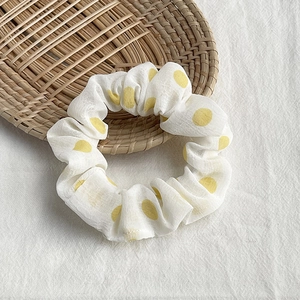 Detailed macro view of a white chiffon scrunchie with yellow polka dots on a wooden tray