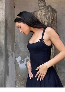 Detail of black sleeveless A-line dress with bow straps against concrete wall