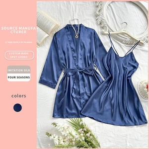 Flat lay of navy blue silk-like satin pajamas set with robe and camisole on white bed
