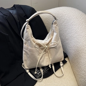 Versatile beige suede shoulder bag with a bow detail on a stylish sofa setting