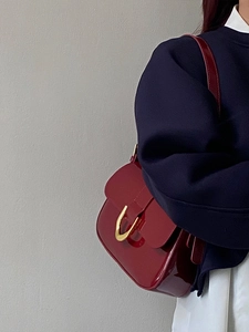 Retro wine red patent leather shoulder bag with gold horseshoe buckle worn by a model