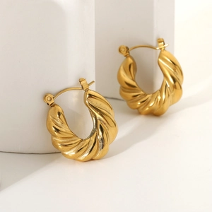 Detailed view of golden croissant hoop earrings with a twisted texture on a white background