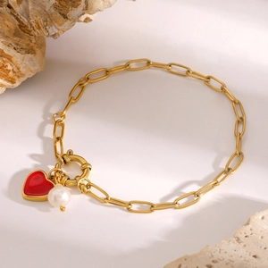 Gold paperclip bracelet featuring a red enamel heart pendant and a white pearl charm