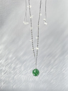 Détail du pendentif gemme verte avec fil d'argent sur un long collier tissé bohème