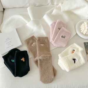Close-up of four pairs of plush winter socks with cute animal embroidery on a cozy blanket