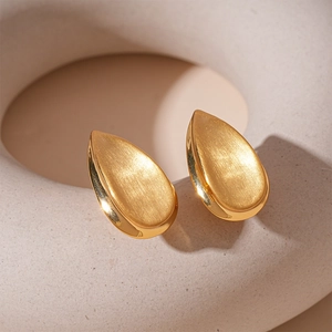 Détail macro de boucles d'oreilles goutte dorées avec texture en métal brossé sur support