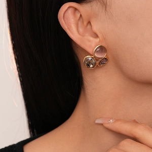 Détail de boucles d'oreilles dorées avec œil-de-chat rose et pierres violettes sur un modèle