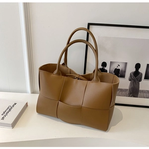 Detail of a brown woven tote bag made of PU leather showing texture on white surface