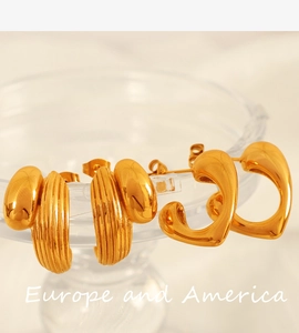 Macro shot of gold C-shaped ribbed earrings and heart studs on a glass rim